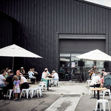 Load image into Gallery viewer, People sitting outside a modern building with large windows and black exterior.
