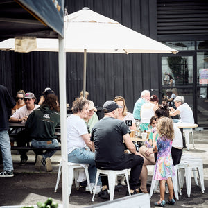 People sitting outdoors under a white umbrella with a 'Strong Organics' sign in the foreground.